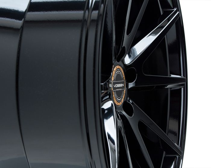 A glossy black wheel rim with multiple spokes radiates from a central hub. The hub bears the text "VOSSEN" and "FORGED." It is set against a plain white background.