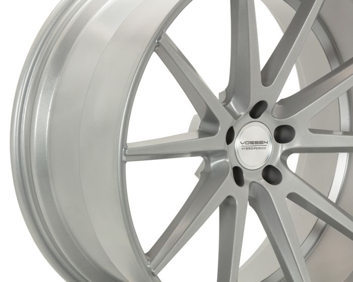 A silver alloy wheel features a multi-spoke design with the center displaying the text "VOSSEN HYBRID FORGED," set against a plain white background.