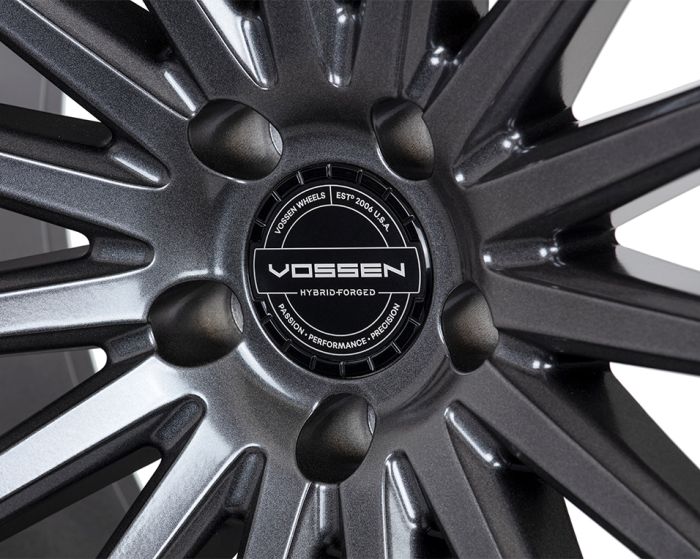 A sleek, dark alloy wheel with multiple spokes features a central emblem. Text reads: "VOSSEN WHEELS EST 2006 U.S.A. VOSSEN HYBRID-FORGED PASSION - PERFORMANCE - PRECISION."