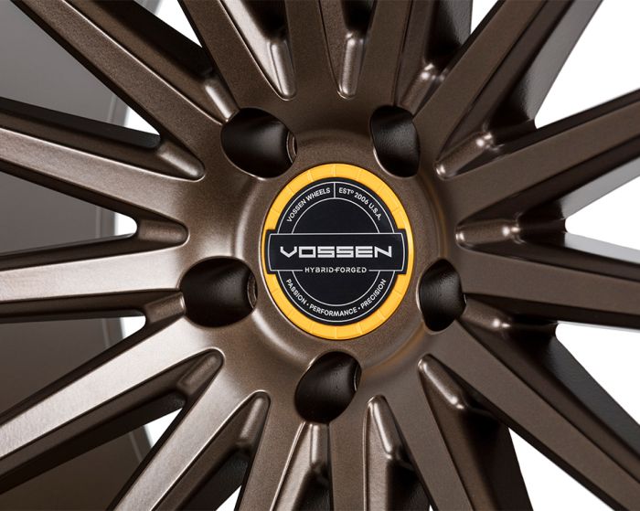 A bronze alloy wheel features multiple spokes radiating from a central hub. The hub displays text: "VOSSEN," "HYBRID-FORGED," "VOSSEN WHEELS," "EST 2006 U.S.A," "PASSION - PERFORMANCE - PRECISION."