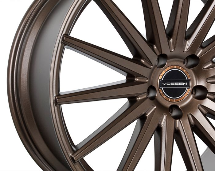 A bronze alloy wheel features multiple slim spokes radiating from a central hub with the 'VOSSEN' logo, set against a plain white background.