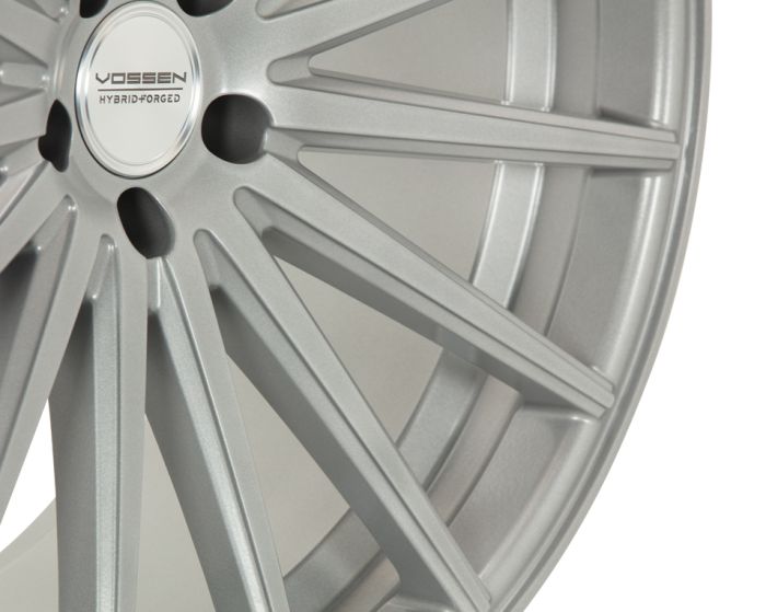 A metallic silver wheel with intricate spokes, featuring the text "VOSSEN HYBRID FORGED" at its center against a plain background.